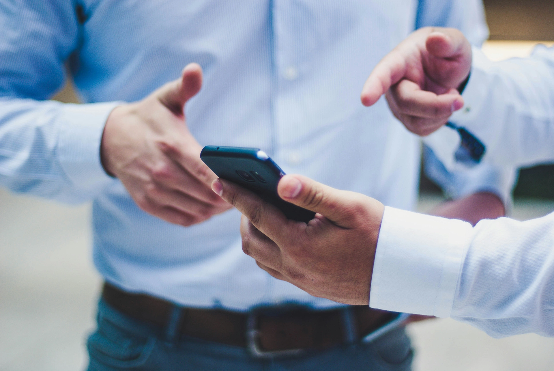 Two individuals in business attire discussing something while looking at a smartphone. One person is holding the phone while the other points at it, suggesting a collaborative decision-making process.